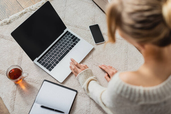 вид сверху женщины с помощью ноутбука возле стеклянной чашки с чаем и смартфоном с чистым экраном 