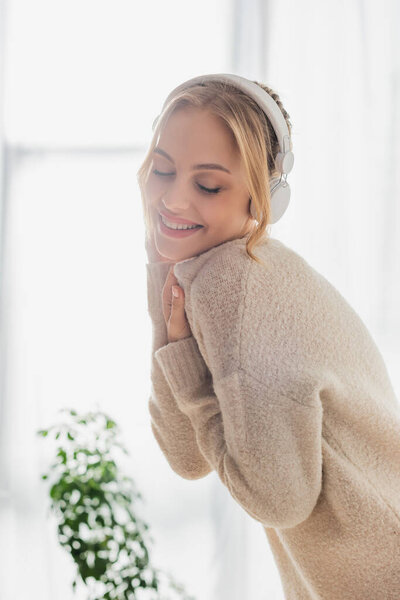 pleased young woman listening music in wireless headphones while having fun at home 