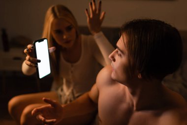 Sarışın kadın, gece sadakatsiz erkek arkadaşıyla tartışırken elinde akıllı telefon tutuyor. 