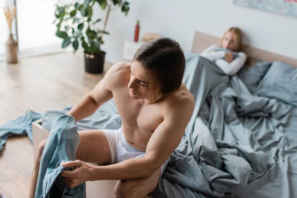 Unfaithful Shirtless Man Wearing Jeans While Sitting Bed Blurred Woman — Stock Photo, Image