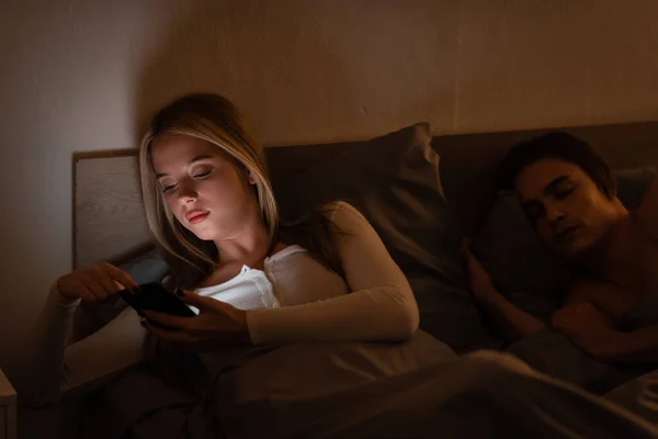 Mulher Infiel Usando Smartphone Lado Namorado Adormecido Noite Traindo Conceito — Fotografia de Stock