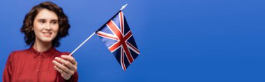 İngiliz bayrağına bakan kıvırcık saçlı mutlu öğrenci mavi pankartta izole edilmiş 