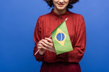 cropped view of happy language teacher smiling while holding flag of Brazil isolated on blue 