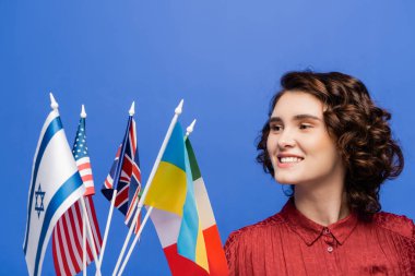 Mutlu genç bir kadın mavi üzerinde izole edilmiş çeşitli ülkelerin bayraklarına bakıyor.