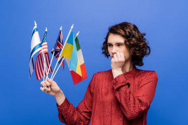Mavi üzerinde izole edilmiş farklı ülkelerin bayraklarına bakarken düşünceli kadın yüz yüze el ele tutuşuyor.