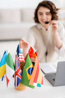 Laptop yakınındaki çeşitli uluslararası bayrakların seçici odak noktası ve evde çalışan bulanık dil öğretmeni