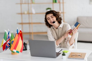 Online ders sırasında uluslararası bayrakların yanındaki dizüstü bilgisayarda kulaklık takan kaygısız dil öğretmeni. 