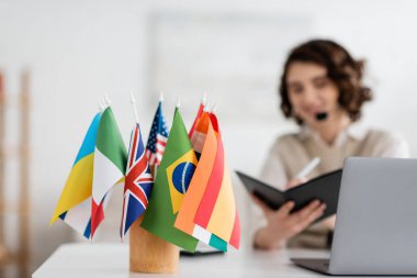 selective focus of international flags near language teacher writing in notebook during online lesson at home clipart