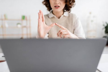 cropped view of woman teaching sign language alphabet near blurred laptop at home clipart