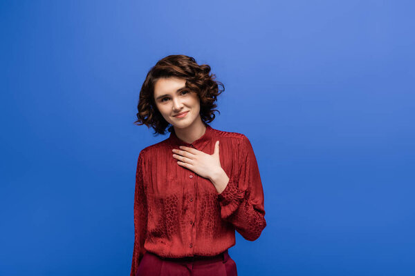 благодарный учитель языка с короткими вьющимися волосами, держась за руку на груди изолированы на синий 