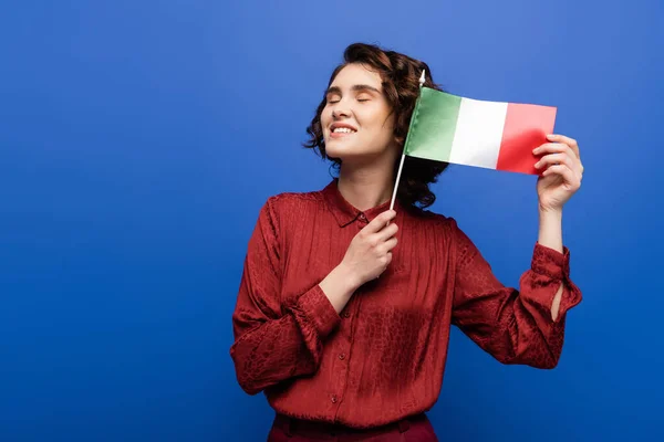 stock image pleased language teacher smiling while holding flag of Italy isolated on blue 