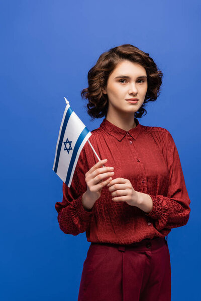 young and serious language teacher with flag of Israel looking at camera isolated on blue