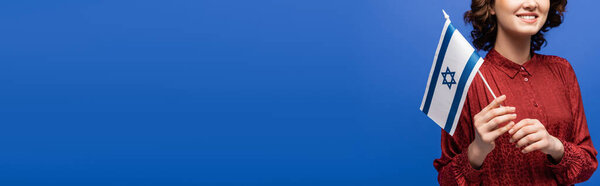 partial view of happy language teacher in red blouse holding flag of Israel isolated on blue, banner