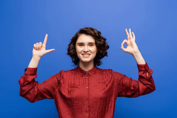 stock image pleased teacher smiling at camera and showing alphabet letters on sign language isolated on blue
