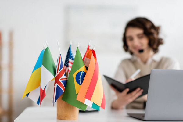 селективный фокус международных флагов рядом с языковым учителем, пишущим в блокноте во время онлайн урока дома