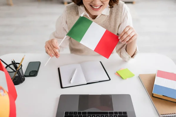 在家里桌上的设备和笔记本旁边挂着意大利国旗的笑容满面的语言老师的照片 — 图库照片