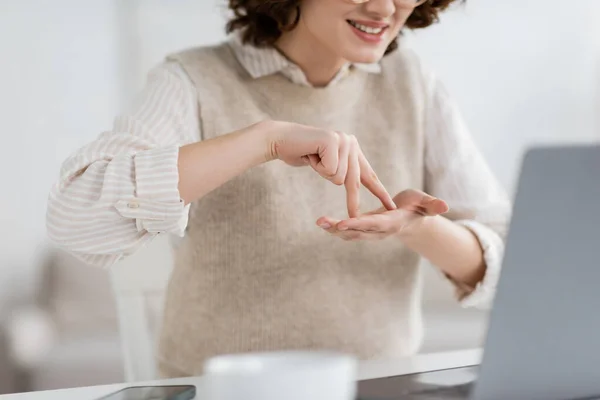 ラップトップでオンラインレッスン中に手話を教えている間にスタンドワードを示す笑顔の女性のクロップドビュー — ストック写真