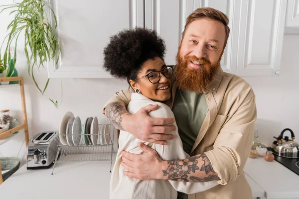Positivo Tatuato Uomo Abbracciare Africano Americano Fidanzata Guardando Fotocamera Cucina — Foto Stock