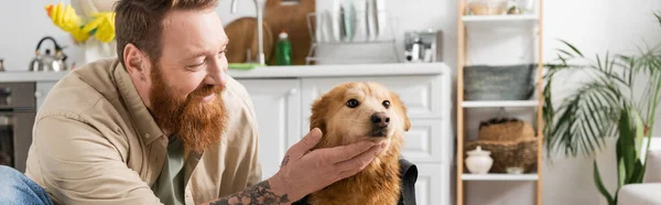 一个快乐的男人 带着胡子 在厨房里爱抚狗 挂着横幅 — 图库照片
