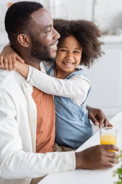 Kıvırcık Afrikalı Amerikalı kız mutlu babasına sarılırken gülümsüyor. 