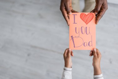 top view of cropped african american child holding greeting card with i love you dad lettering near man on fathers day  clipart