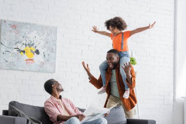 Heyecanlı Afrikalı Amerikalı baba ve çocuk evde gazete okuyarak büyükbabalarının yanında eğleniyorlar. 