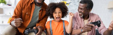 KYIV, UKRAINE - 17 HAZİRAN 2021: Heyecanlı Afro-Amerikan çocuğu evet jestini evdeki joystickli ebeveynlerin yanında gösteriyor, pankart 