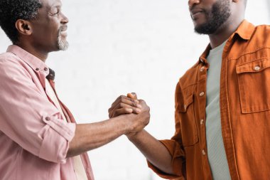 Smiling african american man holding hand of adult son at home clipart