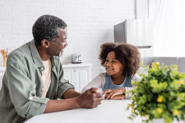 Gülümseyen Afro-Amerikan büyükbabası evde, mutfakta torunuyla konuşuyor. 