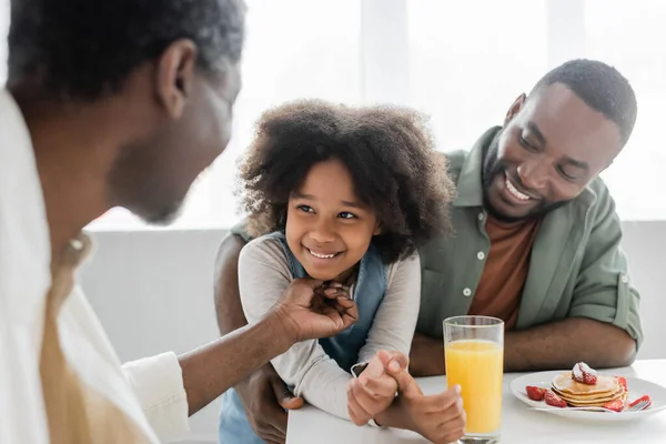 アフリカ系アメリカ人の祖父が家族の朝食中に明るい息子の近くで幸せな孫娘をくすぐる — ストック写真