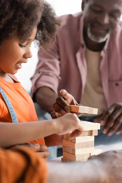 笑顔アフリカ系アメリカ人の女の子遊びます木ブロックゲームともにぼやけたお父さんと祖父上の家 — ストック写真