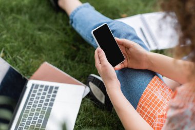 Bilgisayarın yanında otururken elinde boş ekranla akıllı telefon tutan genç bir kadın görüntüsü ve çimlerin üzerinde bir defter. 