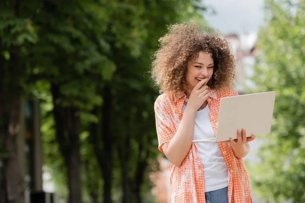 幸せなフリーランスの女性はノートパソコンを持ちながら笑顔で公園で遠隔作業しています — ストック写真