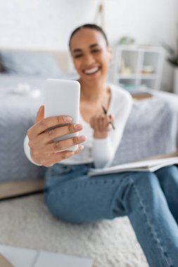 Mutlu ve bulanık Afrikalı Amerikalı öğrenci evde çalışırken akıllı telefondan selfie çekiyor. 