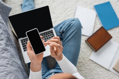 Evden ders çalışırken bilgisayarın yanında boş ekranlı akıllı telefon kullanan Afro-Amerikan öğrencinin üst görüntüsü 
