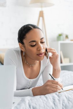 Afro-Amerikan öğrenci akıllı telefondan konuşuyor ve not defterine yazıyor. 