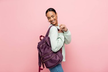 Güzel ve gülümseyen Afrikalı Amerikalı öğrenci pembe bir sırt çantasına bakıyor. 
