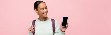 Sırt çantalı gülümseyen Afrikalı Amerikalı öğrenci elinde pembe pankartta izole edilmiş beyaz ekran akıllı telefon tutuyor. 