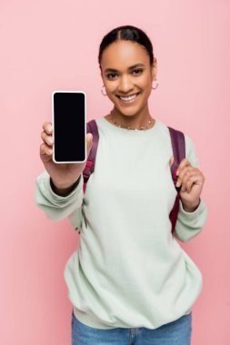 Sırt çantalı bulanık Afrikalı Amerikalı öğrenci elinde pembe ekranlı akıllı telefon tutuyor. 