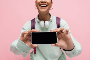 Pembe ekranda izole edilmiş beyaz ekranlı akıllı telefon tutan neşeli Afro-Amerikan kadın manzarası 