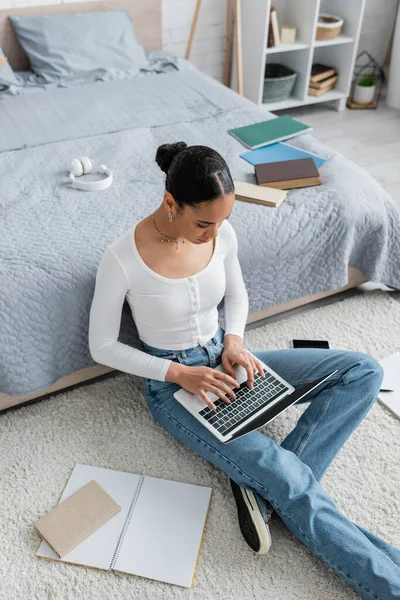 自宅でオンライン学習をしながらノートパソコンのキーボードで入力する若いアフリカ系アメリカ人の学生の高い角度のビュー — ストック写真