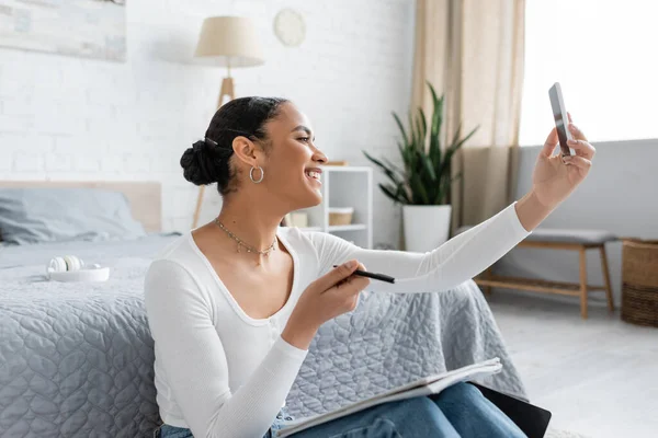 快乐的非洲裔美国学生在家里念书的时候用智能手机自费 — 图库照片