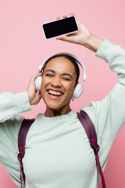 Pembelerden izole edilmiş müzik dinlerken elinde akıllı telefon tutan, kablosuz kulaklıklı Afrikalı Amerikalı kadın. 