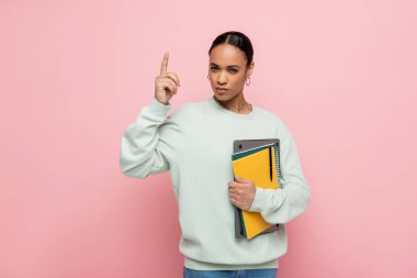 smart african american student holding laptop and notebooks while having idea isolated on pink  clipart