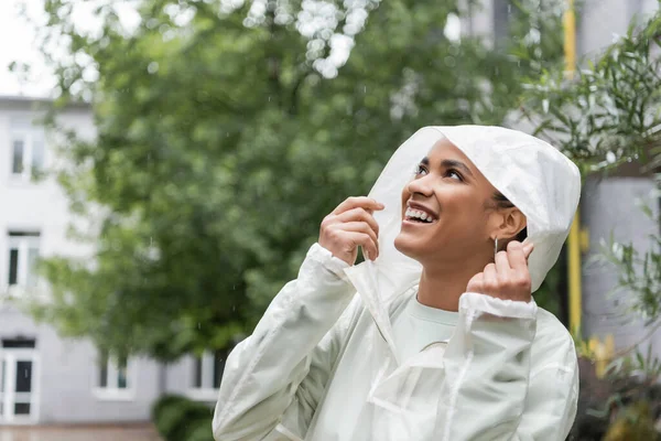 アフリカ系アメリカ人女性が雨の中でフードを見上げて防水レインコートを着て — ストック写真
