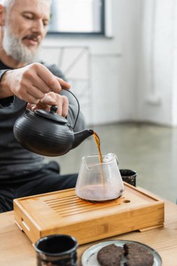 Blurred mature man pouring tea from pot in yoga class  clipart