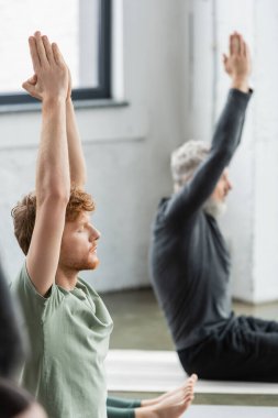 Genç kızıl saçlı adam yoga sınıfında otururken Anjali Mudra yapıyor. 