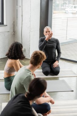 Mature coach showing nostril breathing to blurred group in yoga studio  clipart