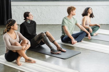 Yoga stüdyosunda minderlerin üzerinde oturan ırklar arası gençler. 