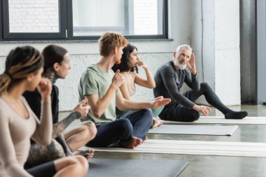 Orta yaşlı koç yoga sınıfındaki çoklu etnik gruplara burun deliği solunumunu açıklıyor. 